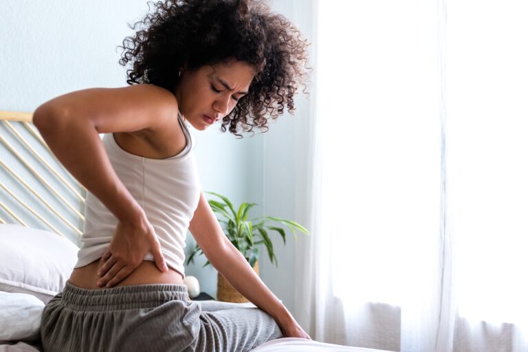 Rear view of woman touching lumbar feeling back pain. Female sitting on bed with back ache.Copyspace